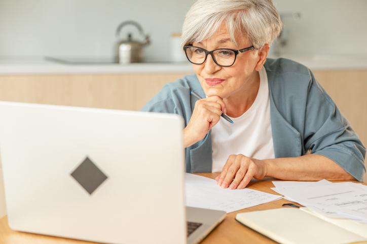 Middle aged senior woman using laptop computer writing notes. Focused mature old woman enjoying working online from home.